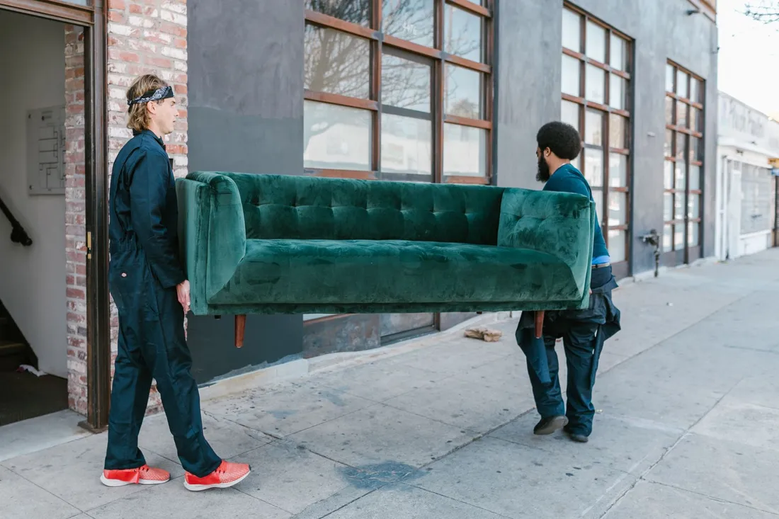 Zwei Umzugshelfer tragen ein Sofa aus einem Wohnhaus